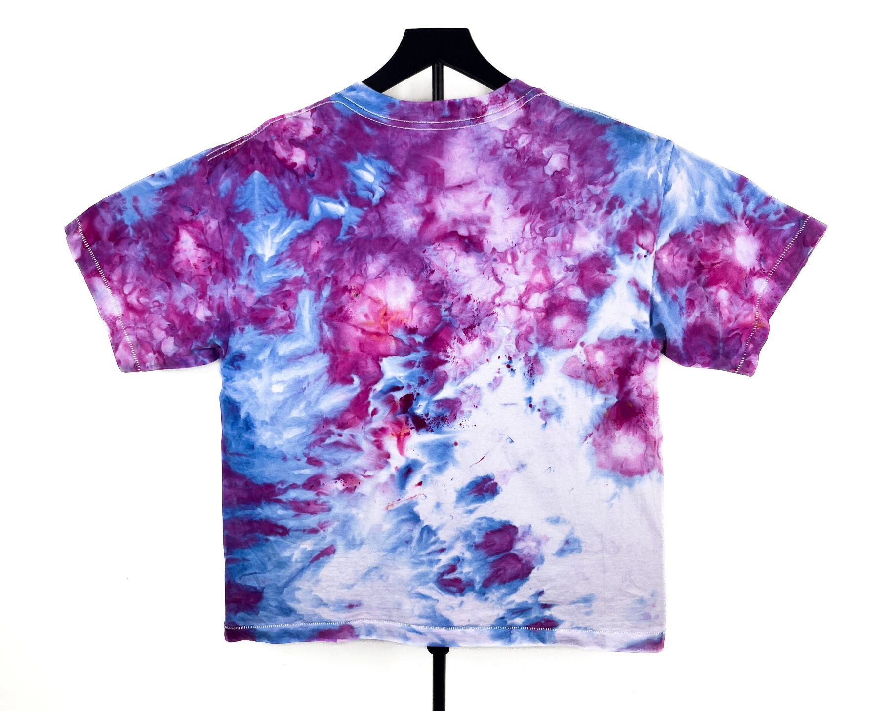 A short-sleeve crewneck t-shirt with a vibrant purple, blue, and pink tie-dye pattern, displayed on a black hanger against a solid white background.