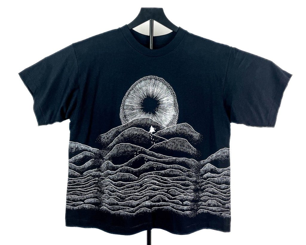 A black short-sleeve t-shirt displayed on a hanger against a white background, featuring a white graphic print of a Shai-hulud mouth from Dune and layered soundwave-style hills.