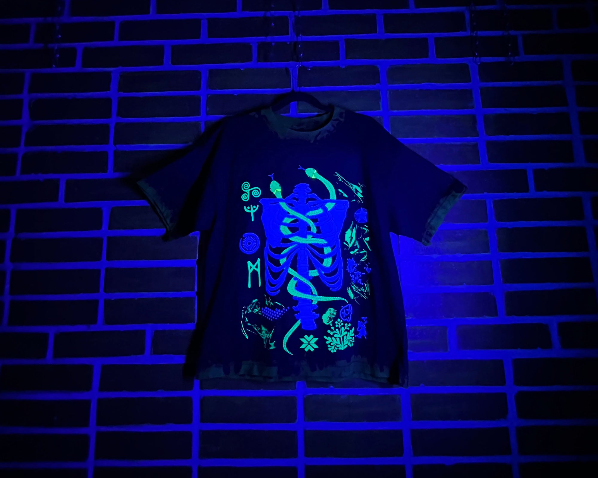 Black t-shirt with glowing green and blue design on a brick wall background
