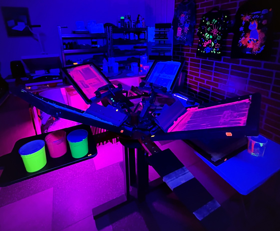 Neon-lit room with tables, chairs, and people gathered around, illuminated by purple and blue lights.