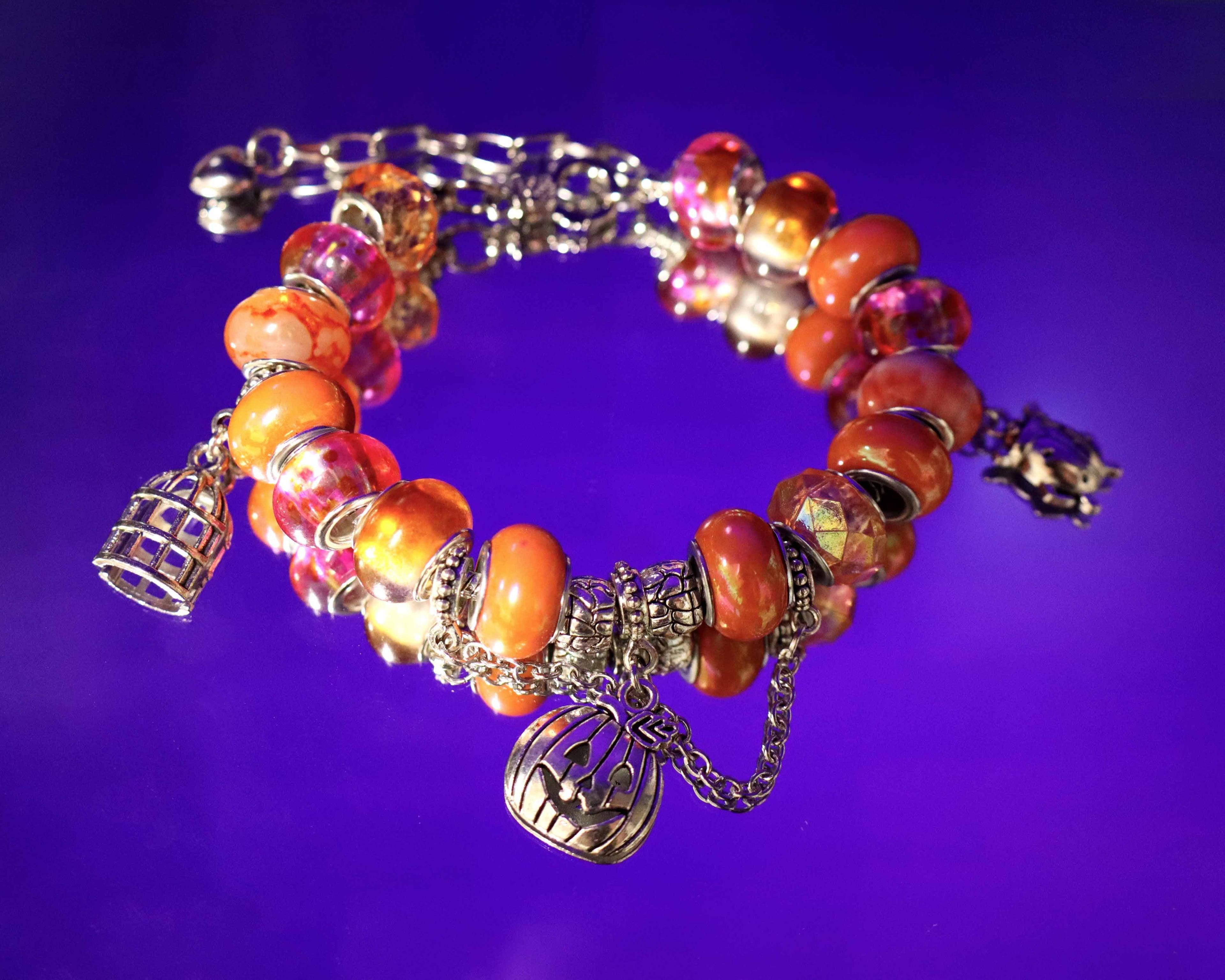 Bracelet with orange beads and silver charms on a purple background