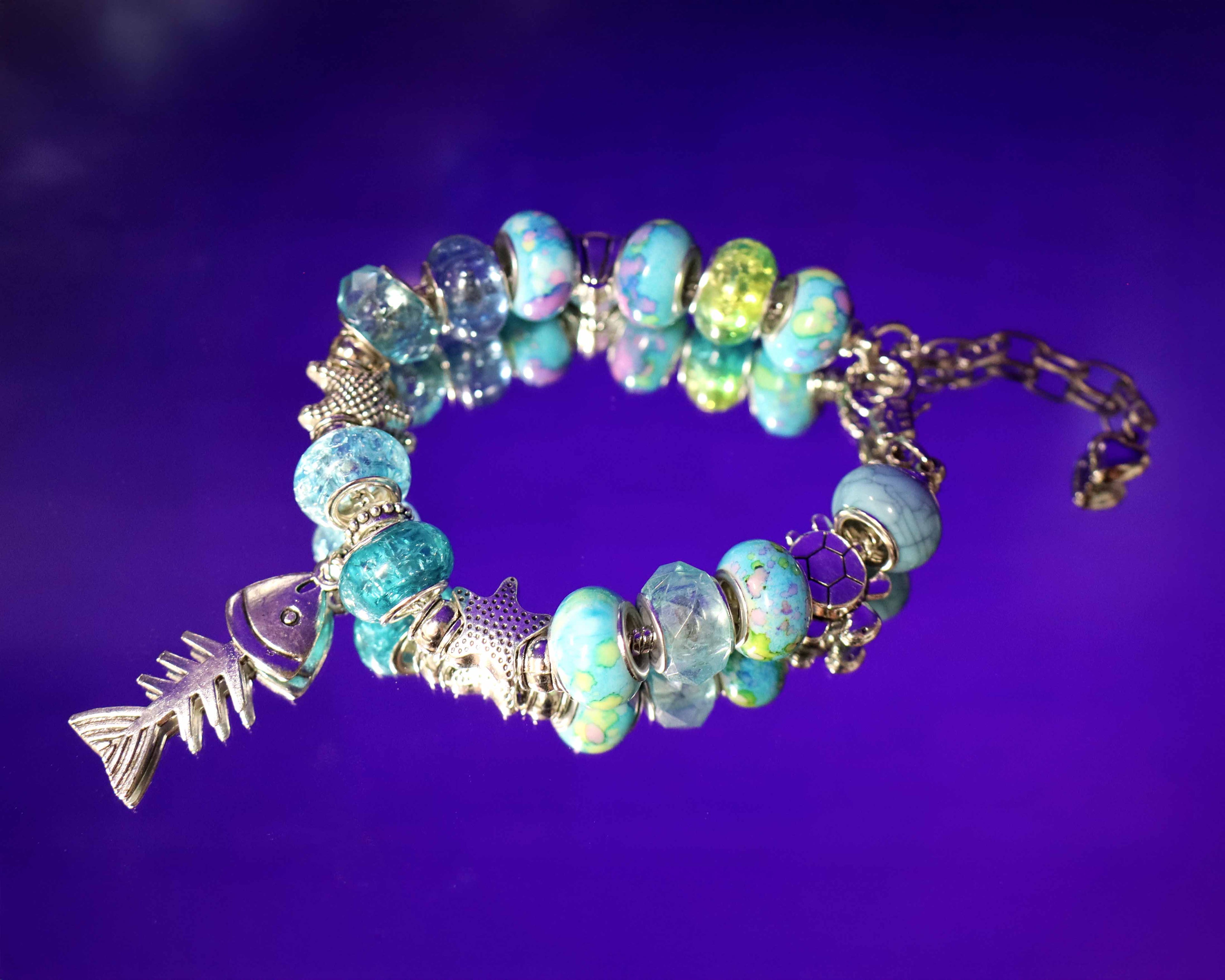 Bracelet with blue beads and fish charm on a purple background