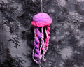 Crocheted jellyfish ornament with pink and purple colors on a black lace background