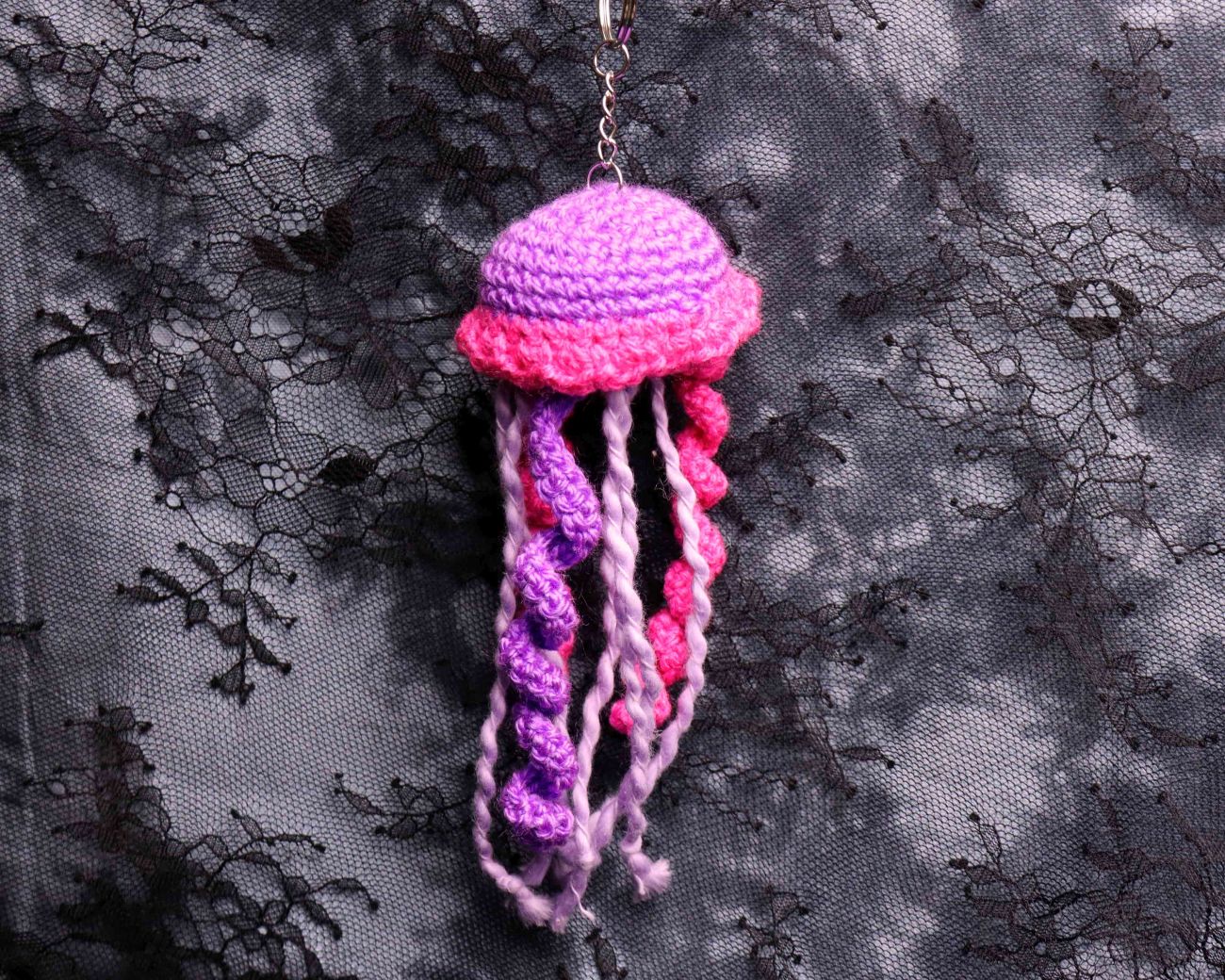 Crocheted jellyfish ornament with pink and purple colors on a black lace background