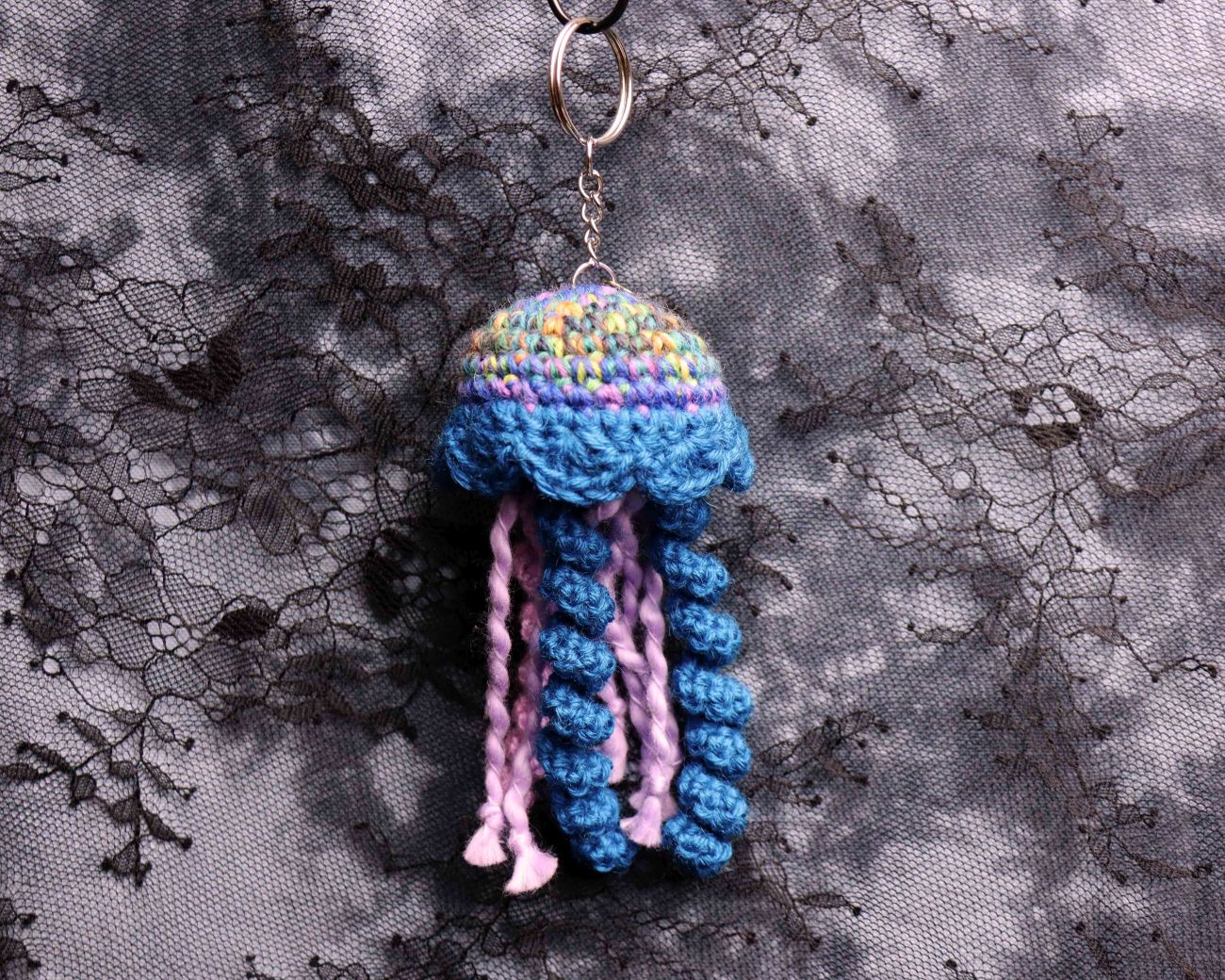 Crocheted jellyfish keychain on a textured gray background