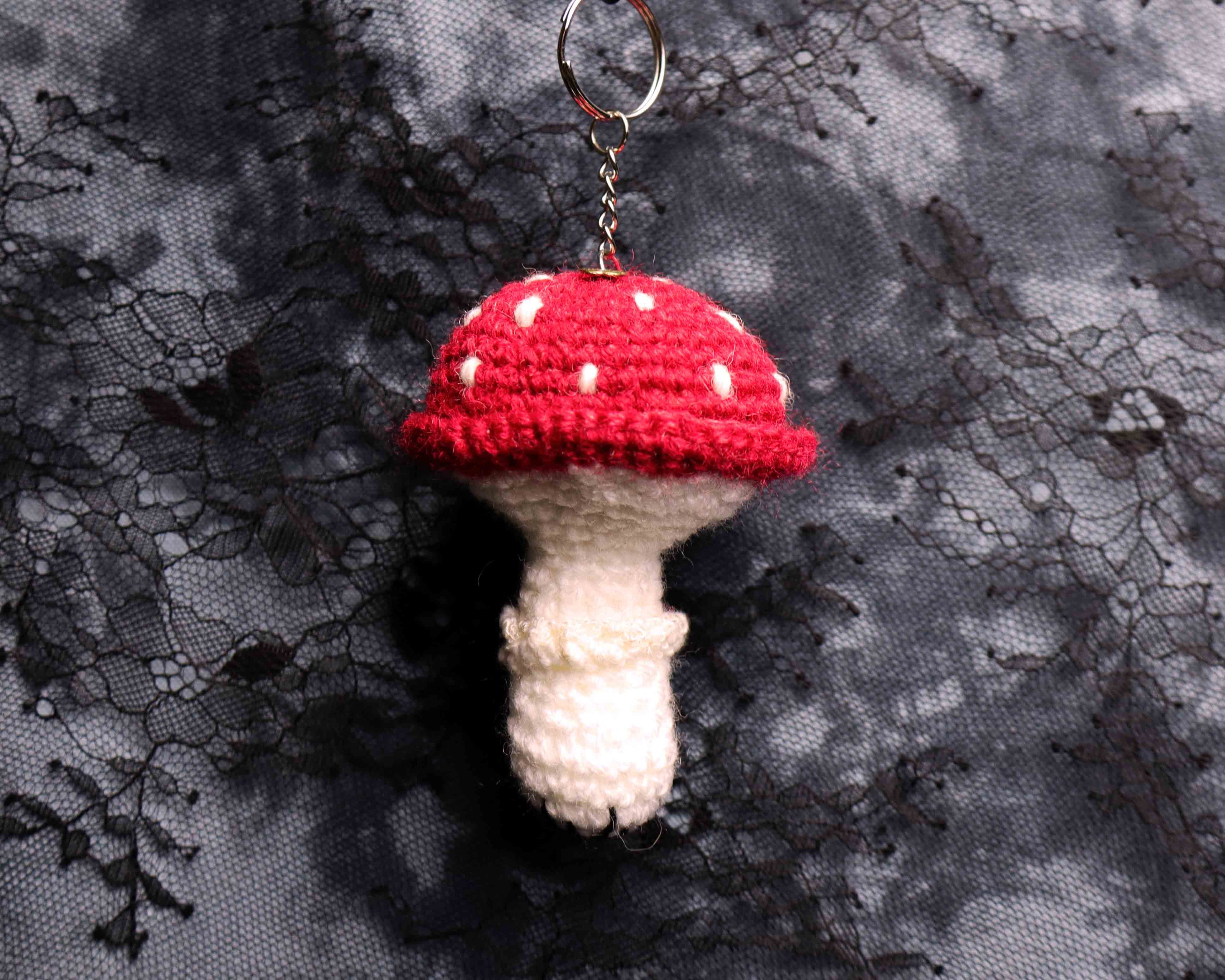 Crocheted mushroom keychain with red cap and white spots on a black lace background