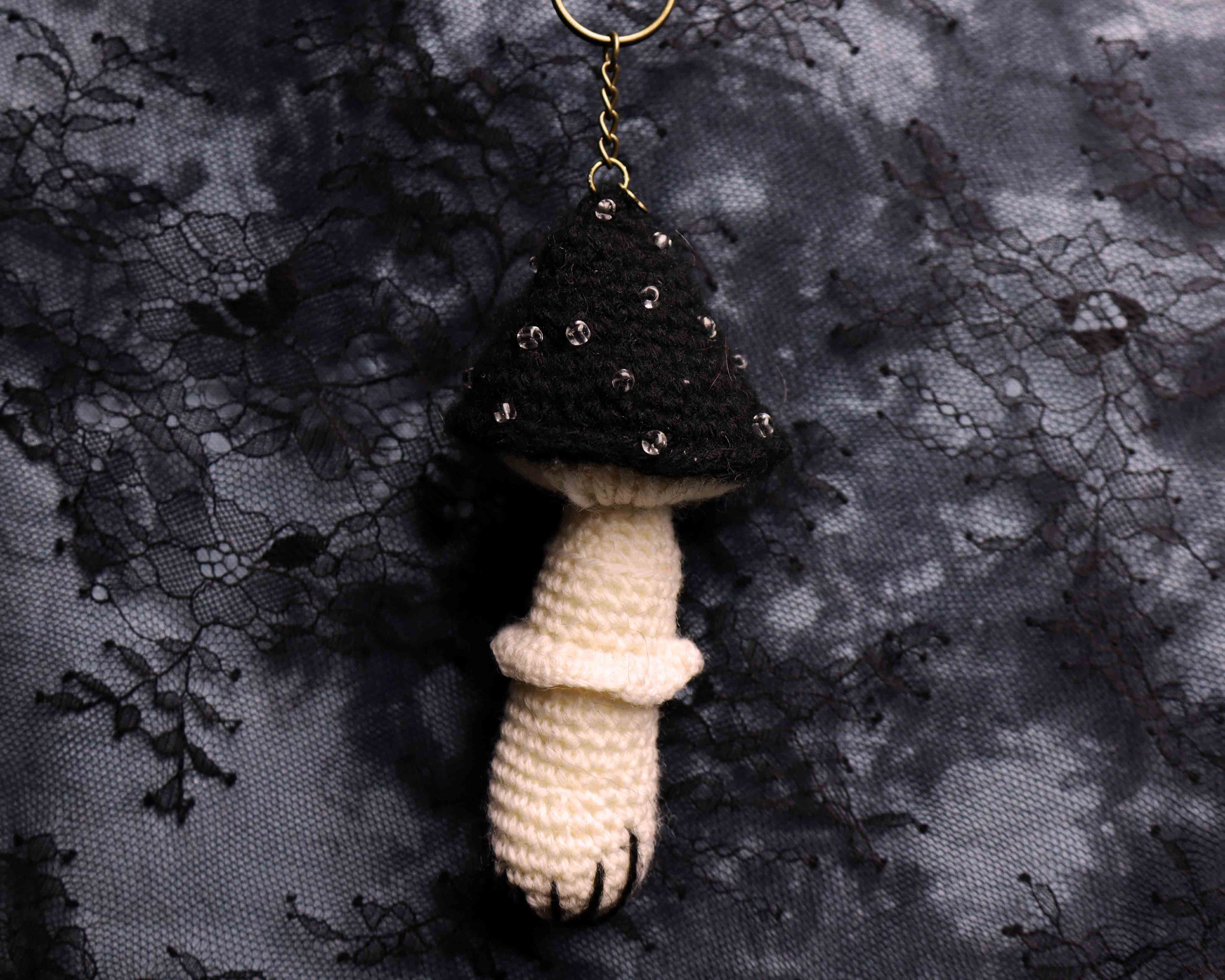 Crocheted mushroom keychain on a dark textured fabric background