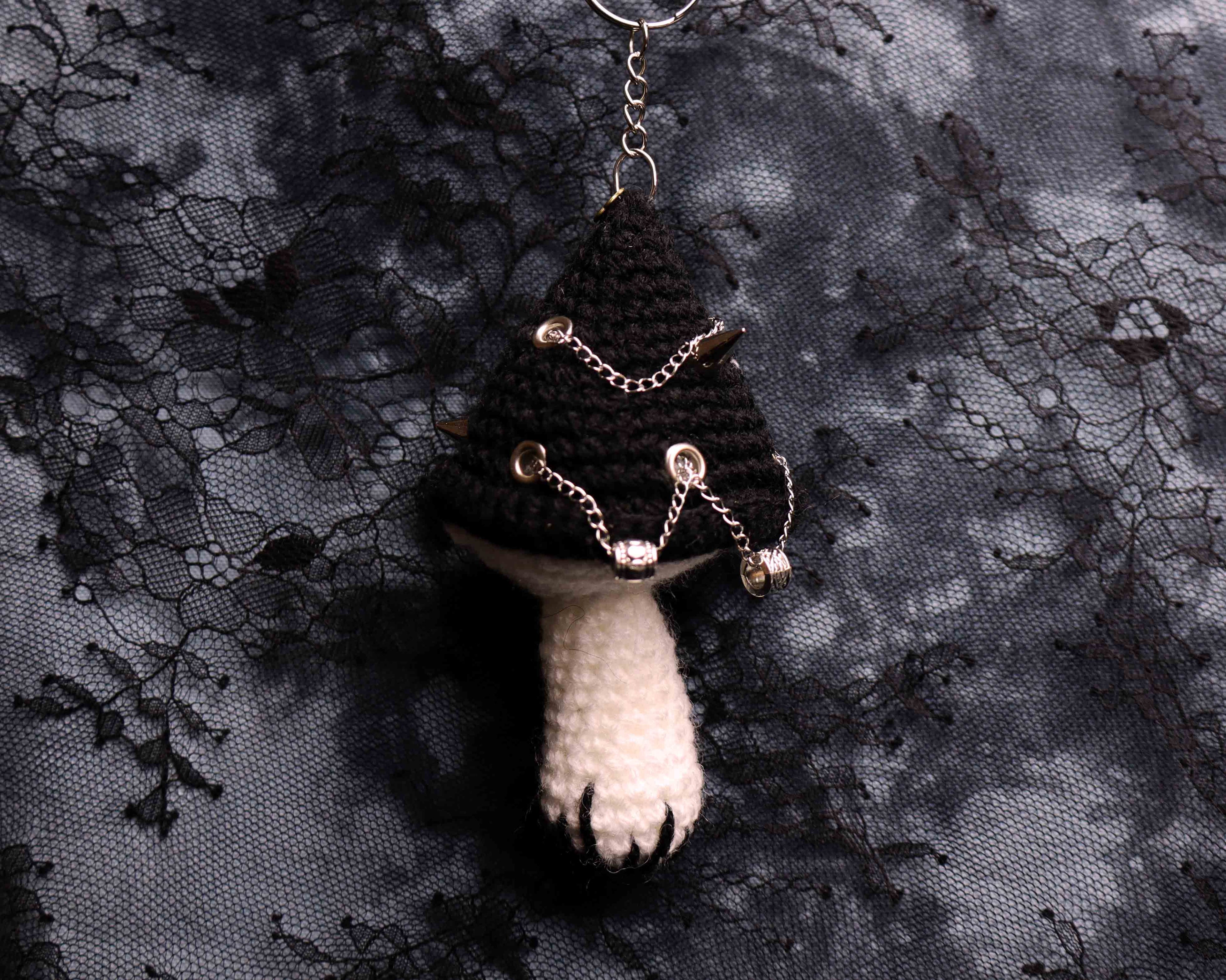 Crocheted keychain with a black cat and white paw on a black lace background