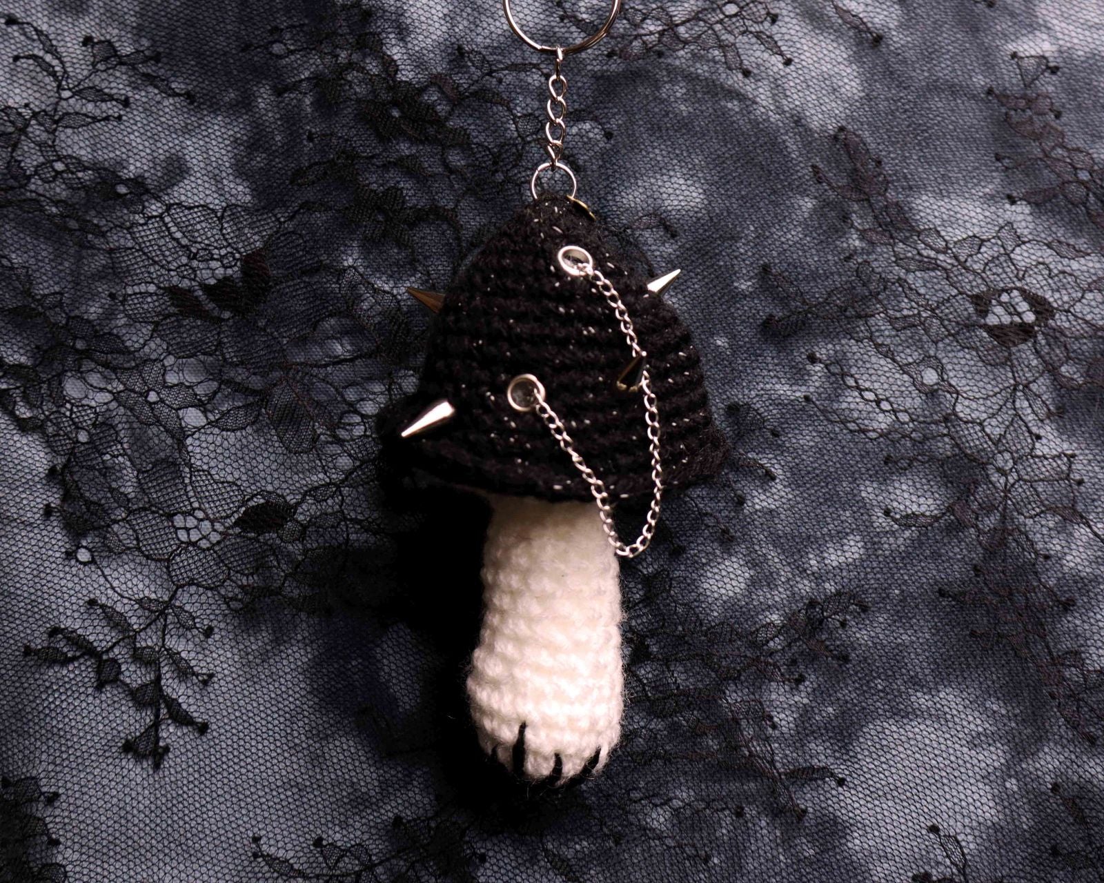 Black and white mushroom-shaped keychain on a dark lace fabric background