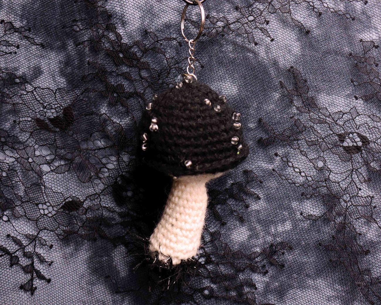 Crocheted black and white mushroom keychain on a textured black lace background