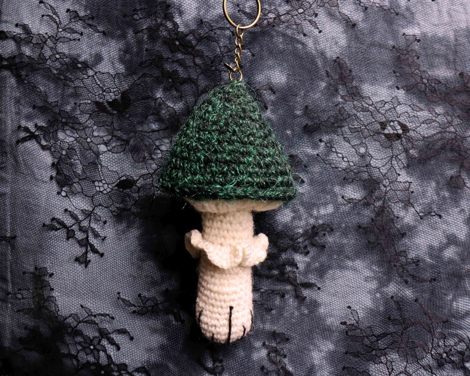 Crocheted mushroom keychain with green cap on a textured black and gray background