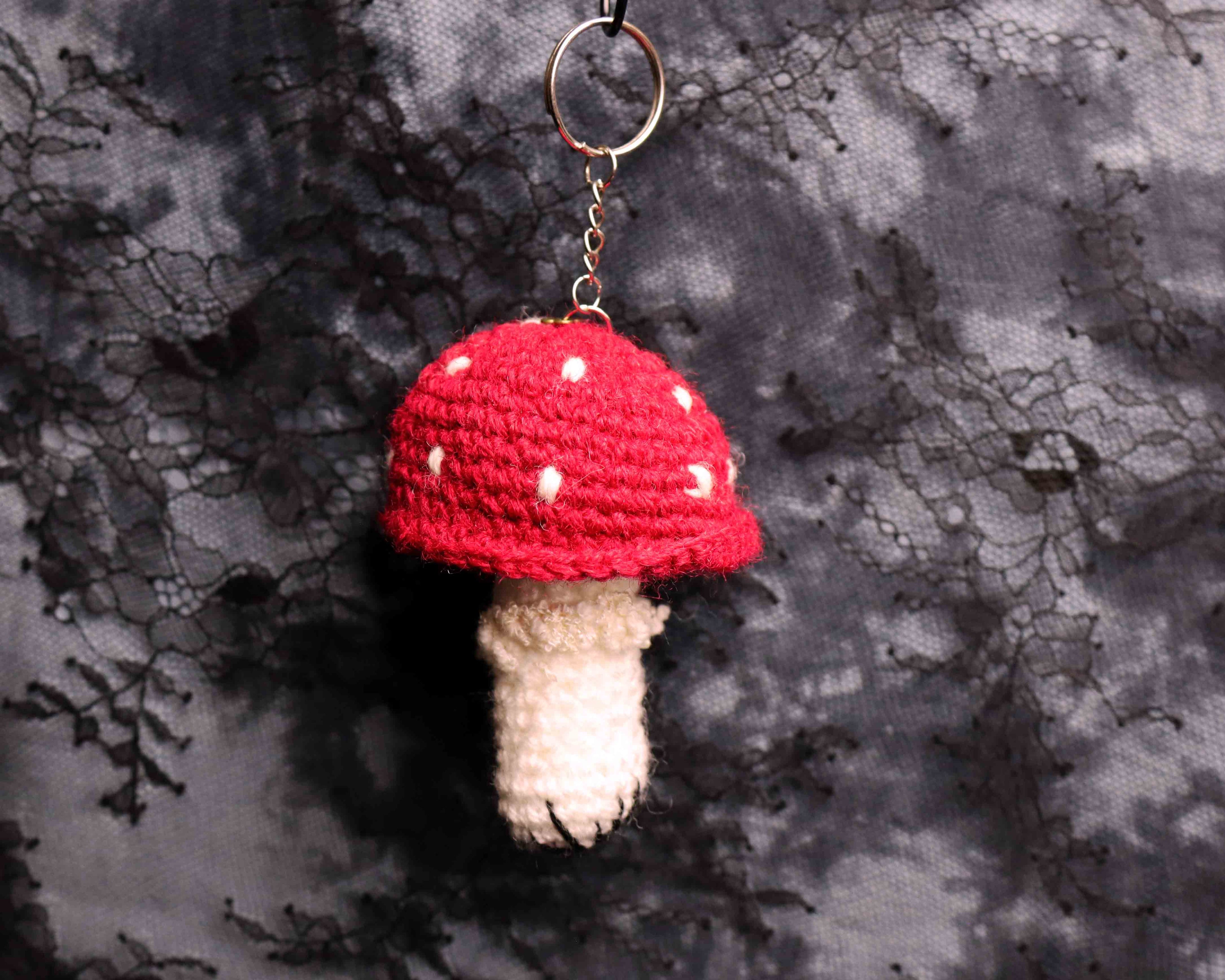Crocheted mushroom keychain with red cap and white spots on a textured gray background