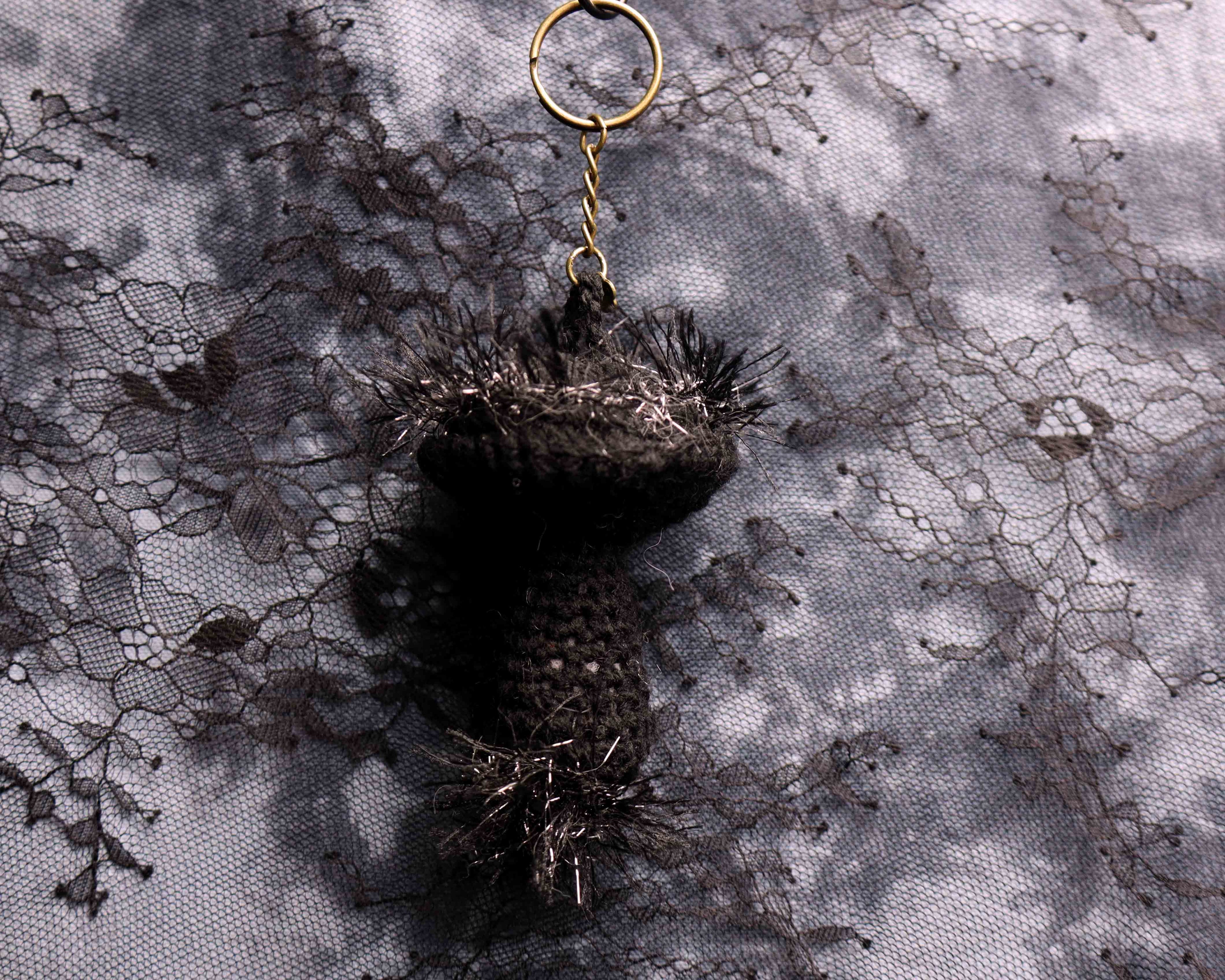Black feathered keychain on a textured gray fabric background