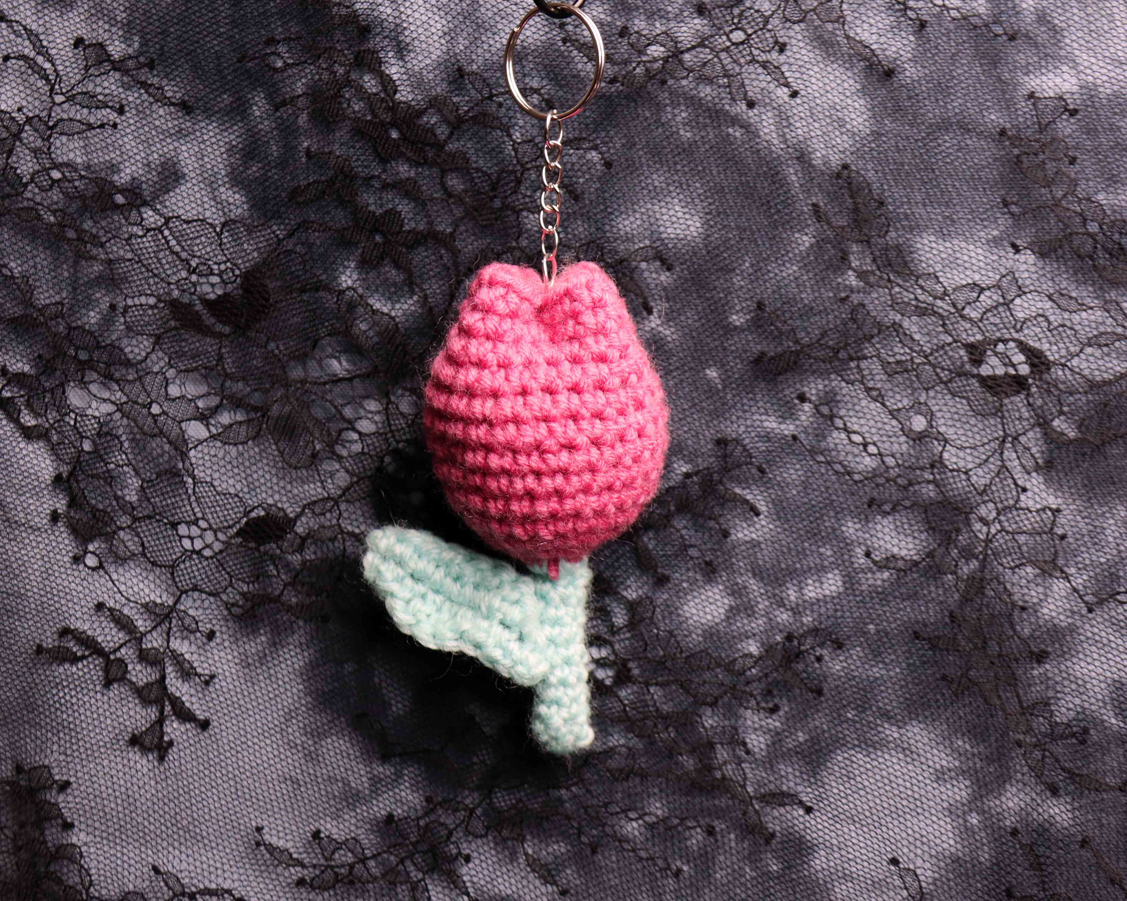Crocheted pink tulip keychain on a textured black and gray background