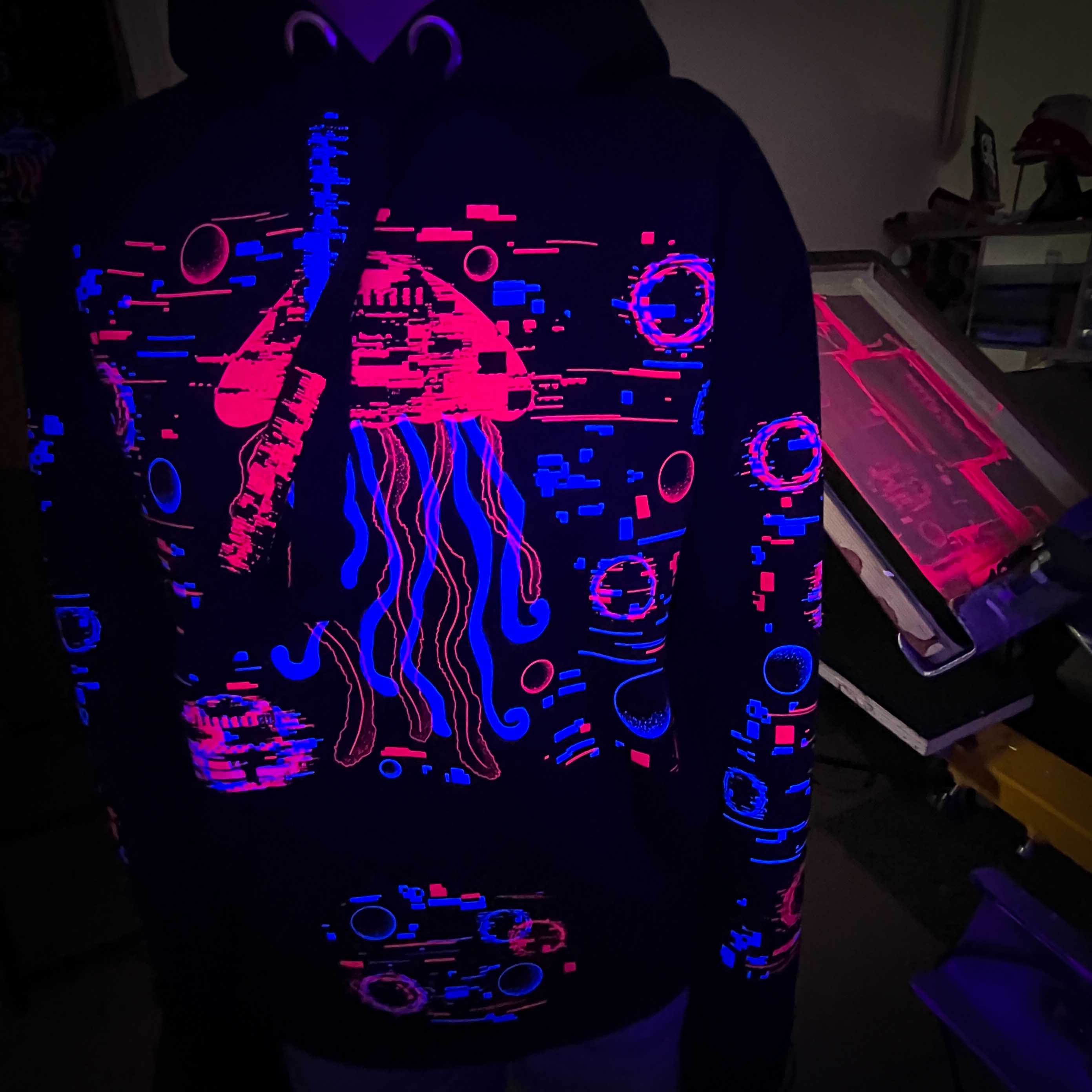 Person wearing a hoodie with a glowing abstract design in black light.