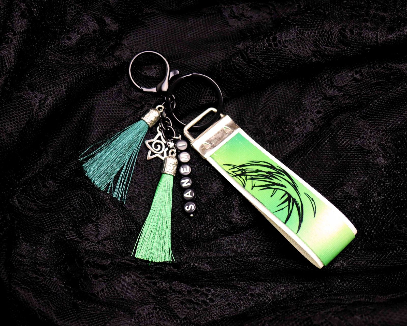 Keychain with green tassel and leaf design on a dark fabric background