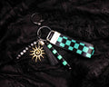 Keychain with green and black checkered strap and sun charm on a dark textured background