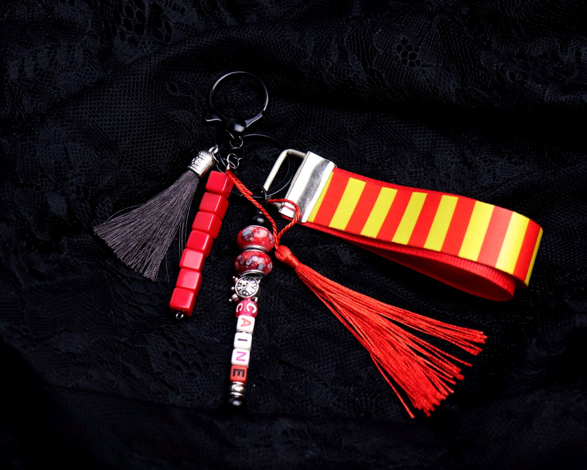 Keychain with red and yellow striped strap, tassel, and decorative charm on a black background